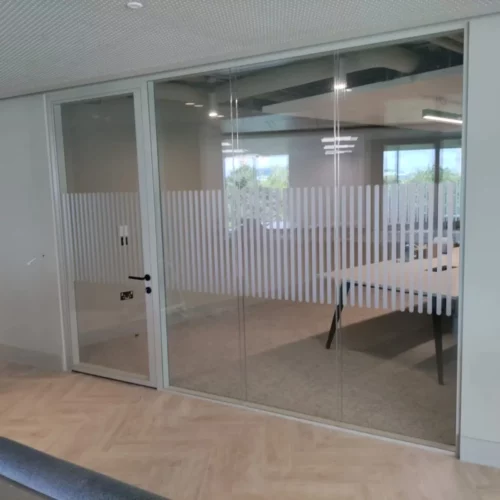A glass-walled office featuring oval-shaped safety dots aligned horizontally. The space is bright with ample lighting and clear visibility through the glass partitions.