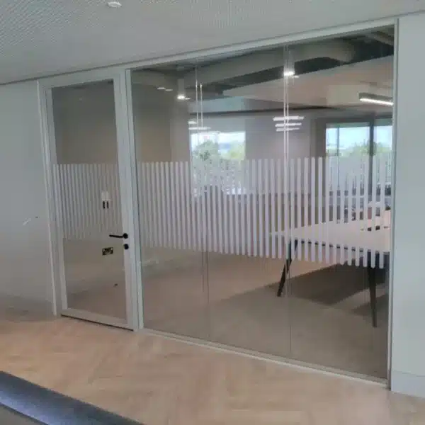A glass-walled office featuring oval-shaped safety dots aligned horizontally. The space is bright with ample lighting and clear visibility through the glass partitions.