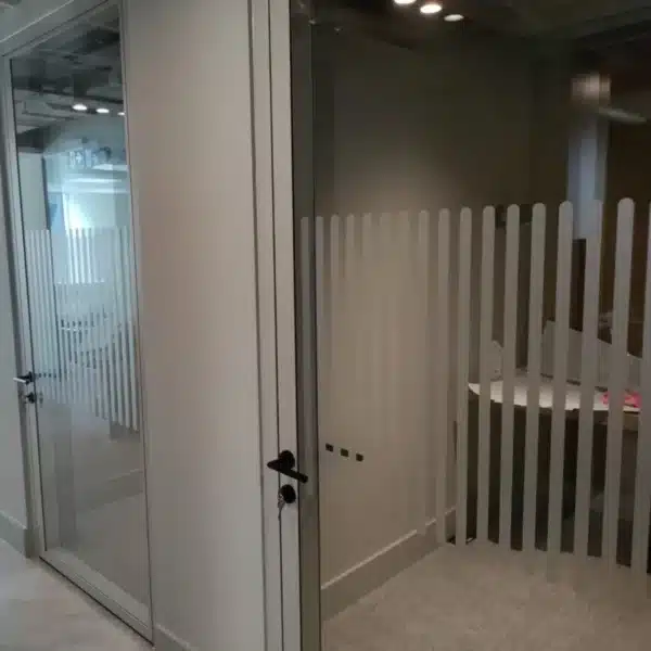 A private office with glass doors and partitions decorated with vertical stripe safety dots. The room is enclosed, providing a distinct and modern design element for privacy and safety.